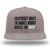 A WeWorkin Snapback Flat Bill Hat in light Heather Grey. "Everybody Wants the Money, Nobody Want$ the WORK." is embroidered front and center in Black and White thread.