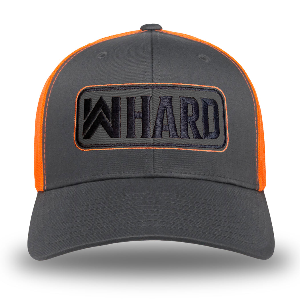 Front view of a Charcoal and Orange Retro Trucker hat. Embroidered with WW HARD "patch" style across the front (WW HARD icon/text in black thread, outer outline in orange thread, inner outline in black thread). Front 2 panels and bill are charcoal (matching charcoal undervisor), side/back mesh panels are orange. Pictured on white background