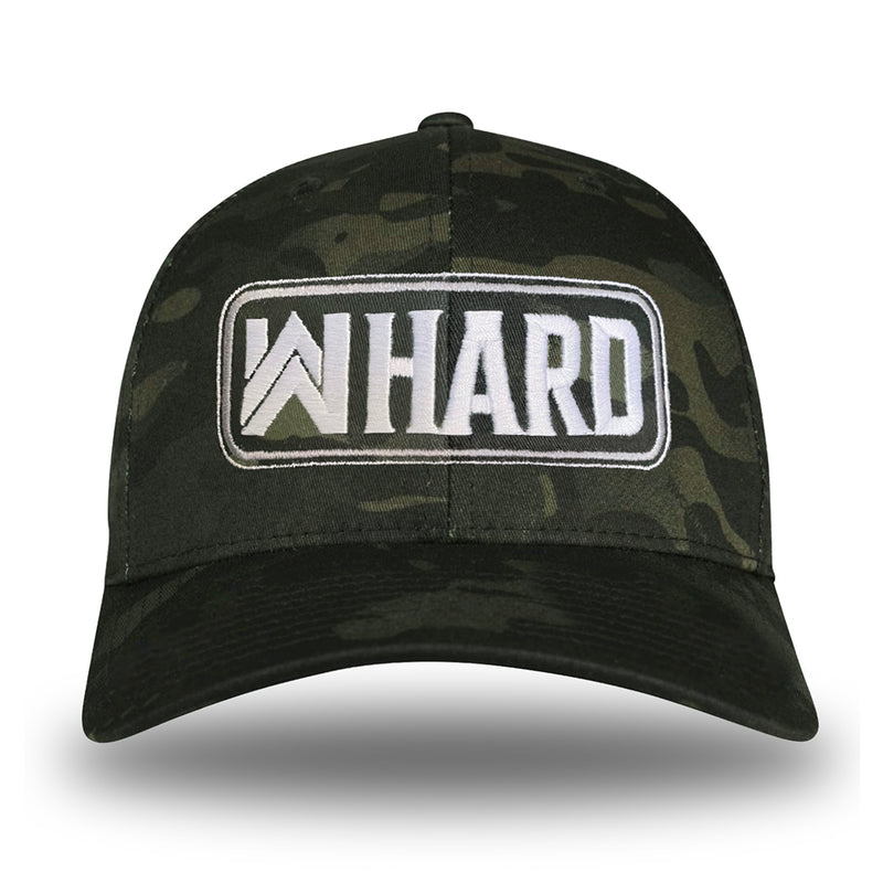 A Multicam® Black Flexfit hat on white background. Embroidered with WW HARD "patch" style across the front (WW HARD icon/text in white thread, outer outline in white thread, inner outline in gray thread). 