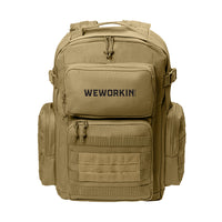 Desert Tan tactical backpack pictured from front on white background. WEWORKIN BRAND logo embroidered in black thread on the top front pocket center. Two side zippered accessory pockets with daisy chain, Top front zippered pocket embroidered, Web carry handle, Lower front zippered pocket with daisy chain and loop panel for badges and patches.