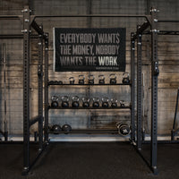 WeWorkin Brand "Everybody Wants the Money, Nobody Wants the WORK." flag displayed on a gym wall. Each flag measures 5'w x 3'h, black background with all grey letters except for the word "WORK" which is in white. White, double-stitched, thicker left edge for durability, (2) gold grommets (one at top left and one at bottom left corners).