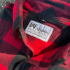 2 We Workin Brand long sleeve Flannel buttoned shirts in Red/Black Buffalo Plaid, folded and placed on asphalt, outdoor background. A close-up view of the white with black thread WW logo block-tag is sewn on the back panel just below the collar and size tag.