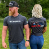 Man and woman pictured outdoors, both wearing the WW FREEDOM tee in Charcoal Grey. He is standing forward and she is showing the back of the tee.