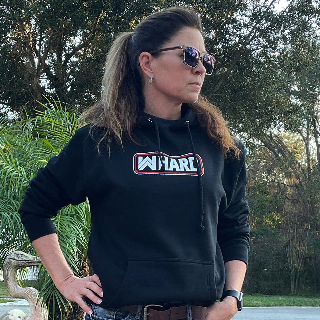 Woman pictured from front wearing a WW HARD Black Hoodie. WW HARD "patch-style" icon printed in red and white, small on center chest. Banded cuffs and waist.