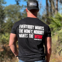 Man pictured from back wearing a WW Black Graphic Tee. "EVERYBODY WANT$ THE MONEY, NOBODY WANTS THE WORK" printed in bold on full back width in white ink, except the word WORK is printed in red for emphasis. (WEWORKIN BRAND APPAREL printed small and lower right just below the full back imprint.) Also wearing a WW HARD Black Camo flexfit hat backwards.