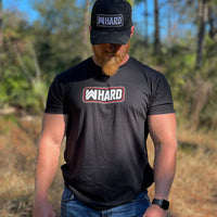 Man pictured from front wearing a WW Black Graphic Tee. WW HARD "patch-style" icon printed in red and white, small on center chest—also wearing a WW HARD Black Camo Flexfit hat.