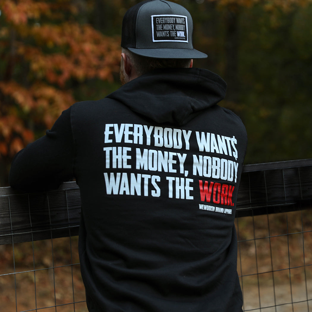 Man pictured from back wearing a WW Black Hoodie. "EVERYBODY WANT$ THE MONEY, NOBODY WANTS THE WORK" printed in bold on full back width in white ink, except the word WORK is printed in red for emphasis. (WEWORKIN BRAND APPAREL printed small and lower right just below the full back imprint.) Hood down on back. (Also wearing a WW Flat Bill Snapback Hat—in Charcoal/Black colors—LG Patch on front, hat backwards.)