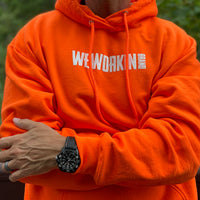 Man pictured close-in from front wearing a We Workin premium Safety Orange hoodie. WEWORKIN BRAND printed on the front chest in white ink.