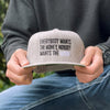Male holding a WeWorkin Snapback Flat Bill Hat in light Heather Grey with both hands. "Everybody Wants the Money, Nobody Wants the WORK." is embroidered front and center in Black and White thread.