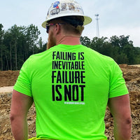 Man on a construction site with a hard hat on, wearing the We Workin Hi-Viz short sleeve tee in Safety Green color. Back is printed with the tagline "Failing is Inevitable Failure is NOT" in black ink. In small text in bottom right corner under the word NOT, is the WW icon and WEWORKIN BRAND APPAREL in white ink.
