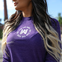 Woman pictured from side/front in a heather purple long-sleeved tee with the text "Not For The Weak" encircling the WeWorkin WW icon. Graphic is imprinted small, in white ink, on upper chest.