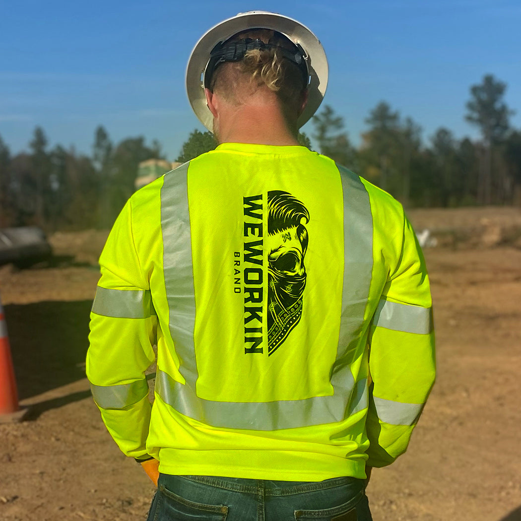 Man pictured from the back on a construction site with a hard hat on, wearing the We Workin Class 3 Mesh Long Sleeve Tee. Back is printed vertically with the WEWORKIN BRAND Half skull with bandana in black ink. (Front is blank)