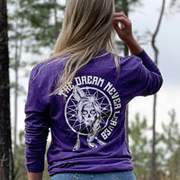 Woman pictured from back in heather purple long-sleeved tee, imprinted with the text "The Dream Never Leaves" and a dreamcatcher/indian graphic in white ink on full back.