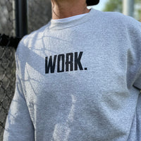 Close up of a man from the front, outdoors, wearing a WW Athletic Grey crewneck sweatshirt. "WORK." printed on center chest in black ink.