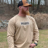Man outdoors pictured from front wearing a WW sand colored long sleeve shirt. WW icon with HARD screen printed in a patch-style design on the center chest in black and white ink. Banded collar and cuffs. (Also wearing a WW Caramel/Black hat with the WW HUNT patch-style graphic embroidered in white and black thread across the (2) center front panels.)