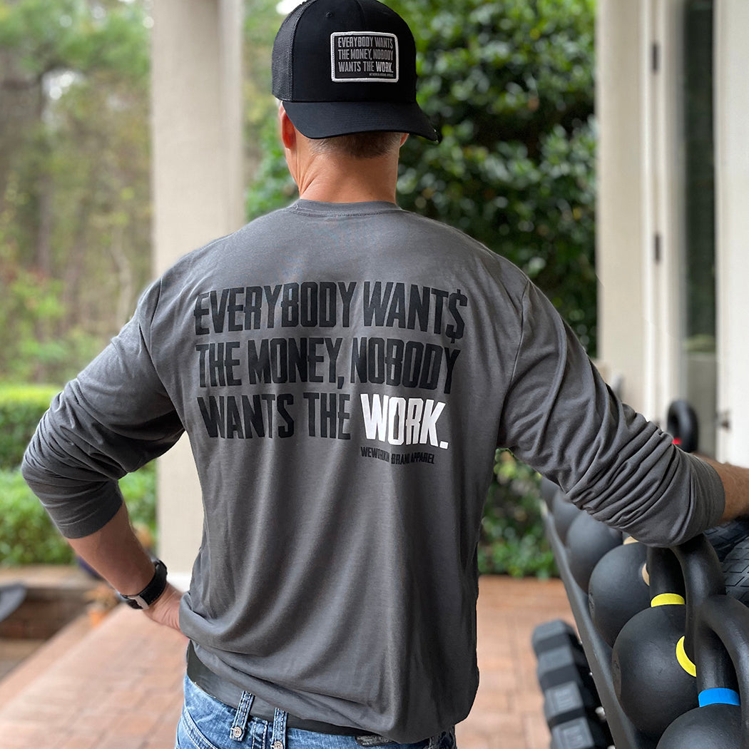 Man pictured from back wearing a WW long sleeve Smoke Grey color shirt. "EVERYBODY WANT$ THE MONEY, NOBODY WANTS THE WORK" printed in bold on full back width in black ink, except the word WORK is printed in white for emphasis. (WEWORKIN BRAND APPAREL printed small and lower right just below the full back imprint.) Also wearing a WW Small Patch EWTM hat backwards.