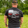 Man outdoors wearing the men's short sleeved "We the Workin" t-shirt in Black. Tattered American Flag printed in White and Red ink, with the text "BUILT BY We the People" printed underneath in white ink. (WEWORKIN BRAND APPAREL with Icon printed small and centered, just below the full back imprint.)