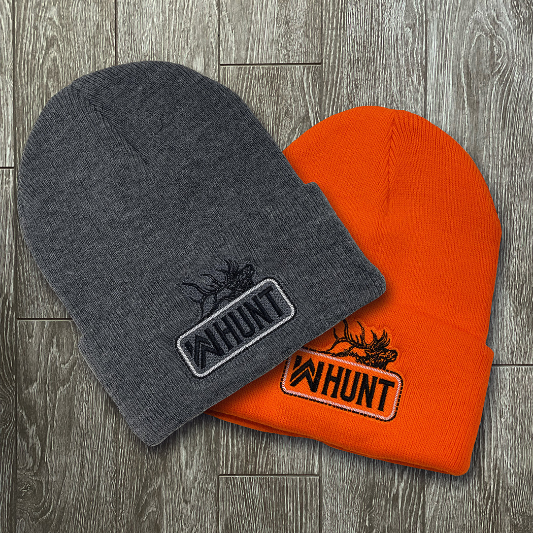 WW HUNT Neon Safety Orange and Dark Heather Grey cuffed beanies on a grey tile background. Embroidered with WW HUNT and ELK image in our signature "patch" style on the folded cuff (WW icon/text/elk graphic in black thread, outer outline in black thread, inner "rope" in white thread). 
