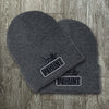 Two WW HUNT Dark Heathered Grey cuffed beanies on a grey tile background. Embroidered with WW HUNT and ELK image in our signature "patch" style on the folded cuff (WW icon/text/elk graphic in black thread, outer outline in black thread, inner "rope" in white thread). 