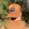 Man wearing a WW HUNT trucker hat in Caramel color, backwards. Embroidered with WW HUNT and ELK in our signature "patch" style across the front (WW icon/text/elk graphic in black thread, outer outline in black thread, inner "rope" in white thread). Front 2 panels and bill are caramel color, side/back mesh panels are caramel color.