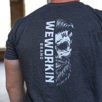 Man pictured from back wearing a We Workin graphic tee in Heather Charcoal Grey color. Short sleeve shirt imprinted with a WeWorkin designed graphic—a large WeWorkin Brand half skull icon (printed in white ink.)